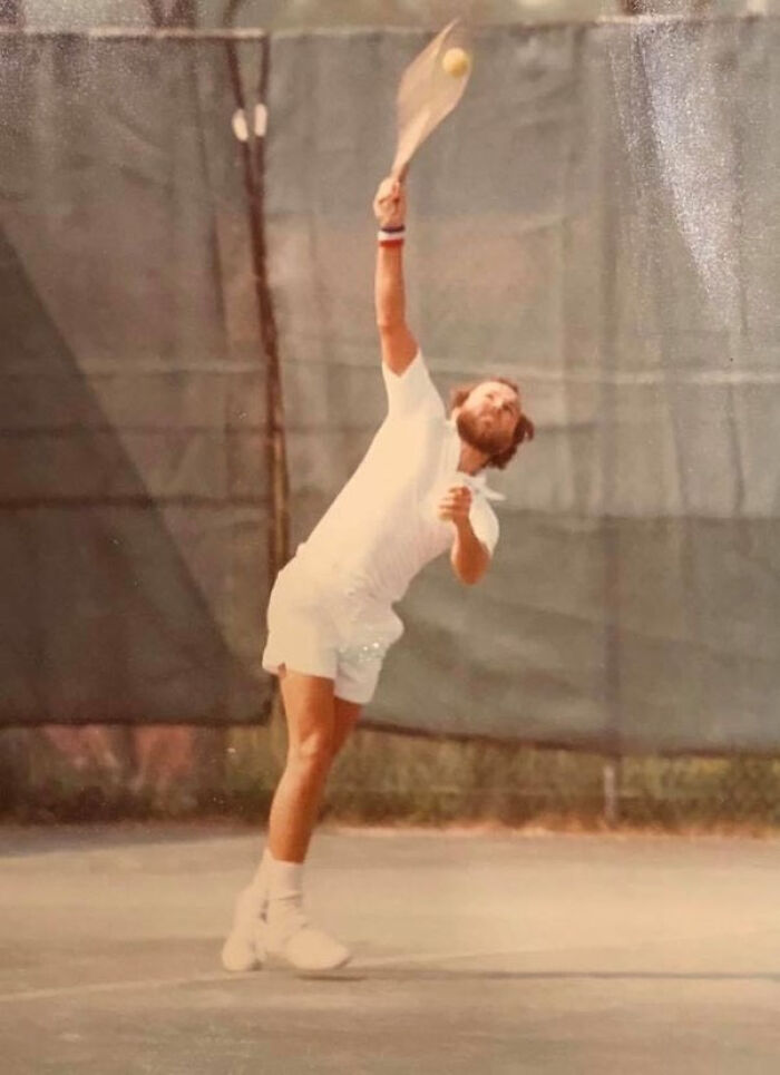 Man serving tennis ball mid-air on outdoor court in vintage photo
