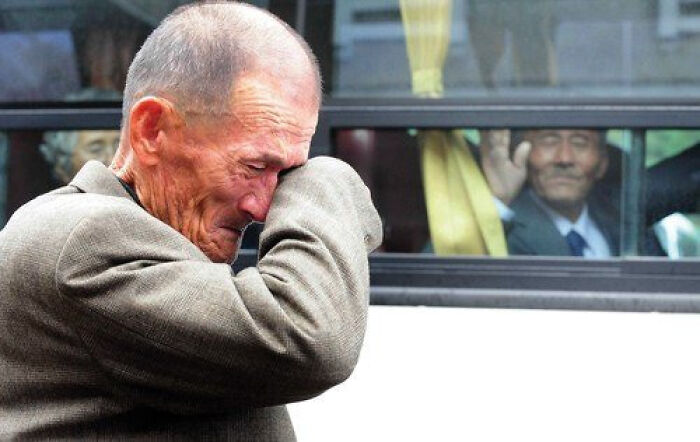 Emotional elderly man crying as another man waves from bus window