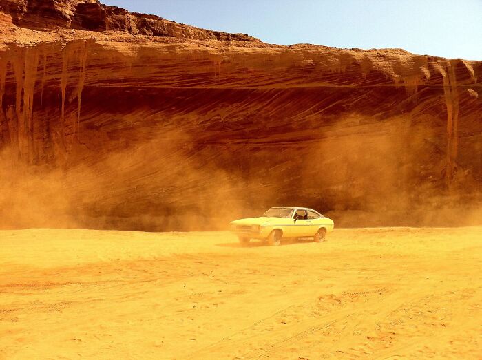 Yellow car driving in dusty desert with stunning views of rocky cliffs