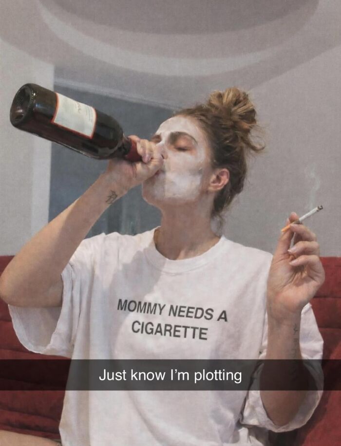 A woman wearing a white t-shirt with the text MOMMY NEEDS A CIGARETTE, drinking wine, a brilliant and bizarre t-shirt.