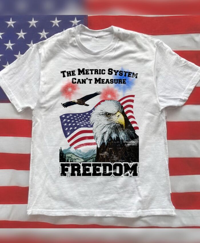 A white T-shirt featuring an eagle, an American flag, and fireworks, with the text The Metric System Can't Measure Freedom, showcasing brilliant T-shirts.