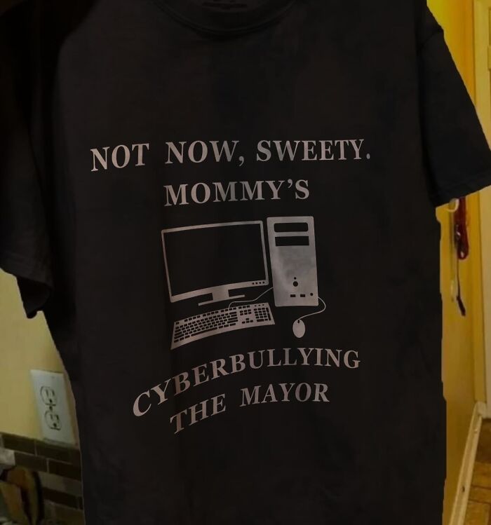 A black T-shirt with the text Not now, sweety. Mommy's cyberbullying the mayor, next to a computer illustration, highlighting brilliant and bizarre T-shirts.
