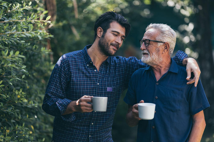 Adult son and elderly father enjoying coffee in garden representing in-laws' visits Adult son and elderly father enjoying coffee in garden representing in-laws' visits