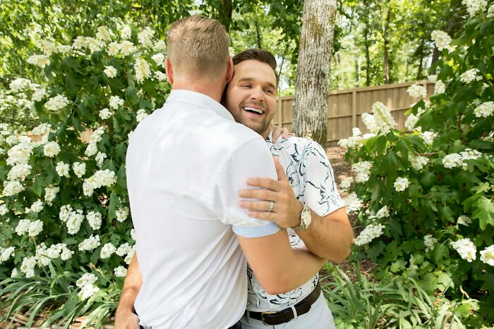 Two men hugging happily outdoors with greenery background