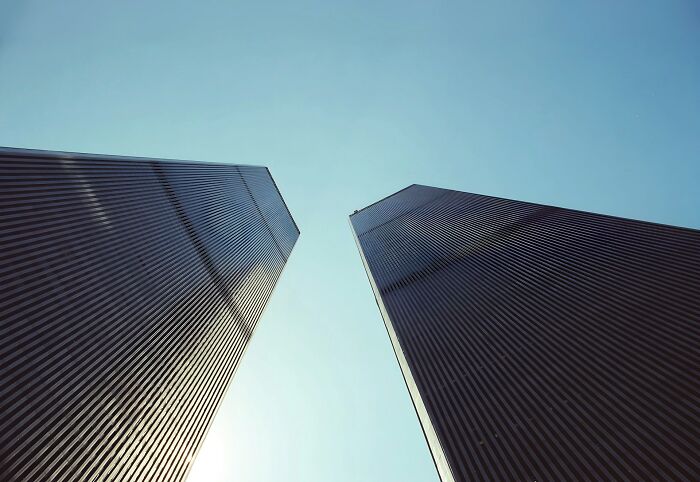 Two dark, imposing skyscrapers rise towards a clear blue sky, evoking a disturbing d***h story.