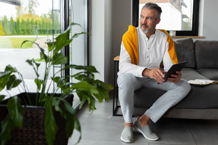 Middle-aged man sitting indoors holding tablet, looking thoughtful Middle-aged man sitting indoors holding tablet, looking thoughtful