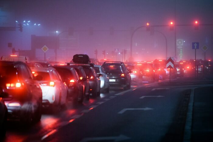Cars with brake lights on in a traffic jam on a foggy night, red streetlights illuminating the scene. An engagement story of chaos.