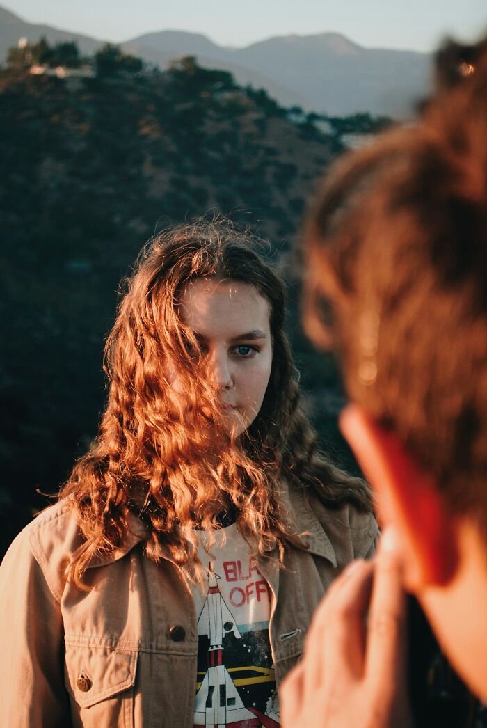 Young woman with curly hair standing outdoors with mountains in background