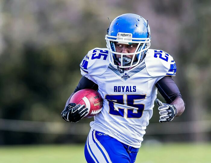 A football player in a blue helmet and white Royals jersey with #25, carrying the ball. Learn cool fascinating facts.