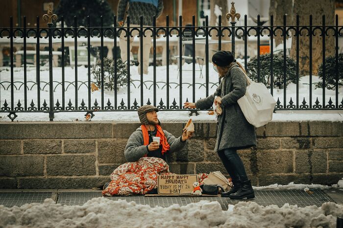 Person giving food to a homeless man on a snowy street highlighting poverty