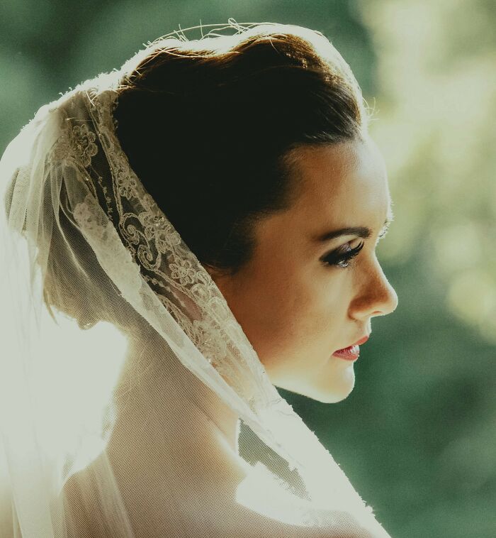Bride in lace veil looking sideways with soft natural light at wedding