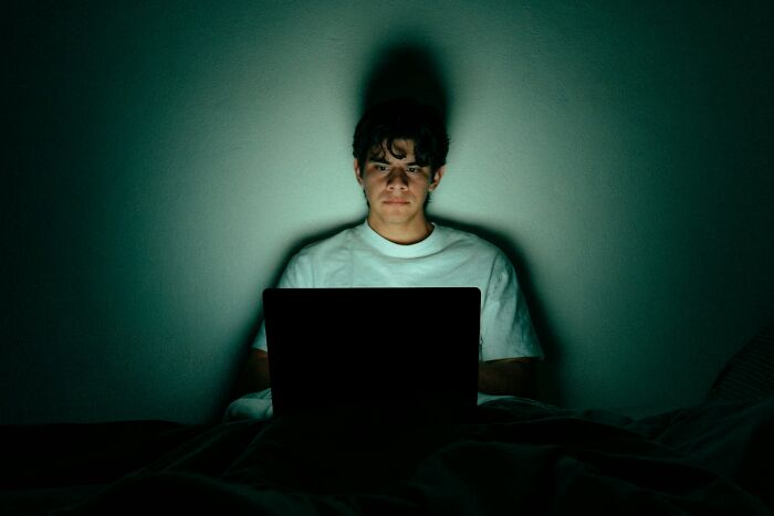 A young man intensely looking at a laptop screen in a dark room, illustrating men suffering and manosphere content.