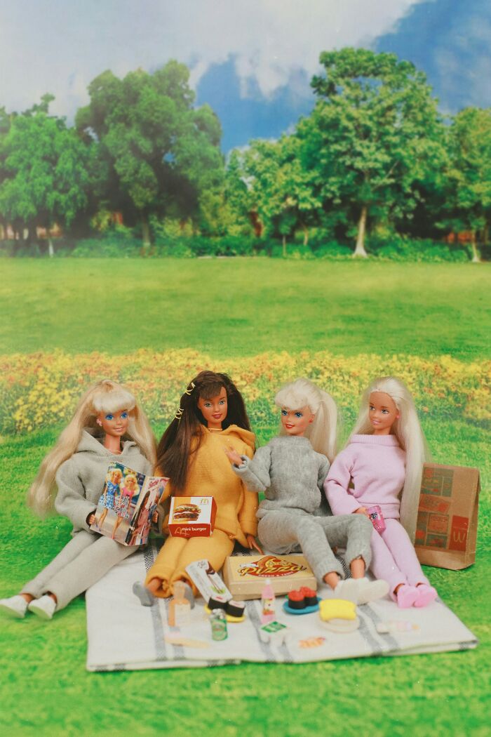 Four dolls having picnic with toy food in park setting