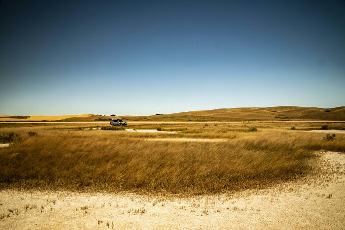 Dry grassland with vehicle driving on dirt road under clear sky geography facts