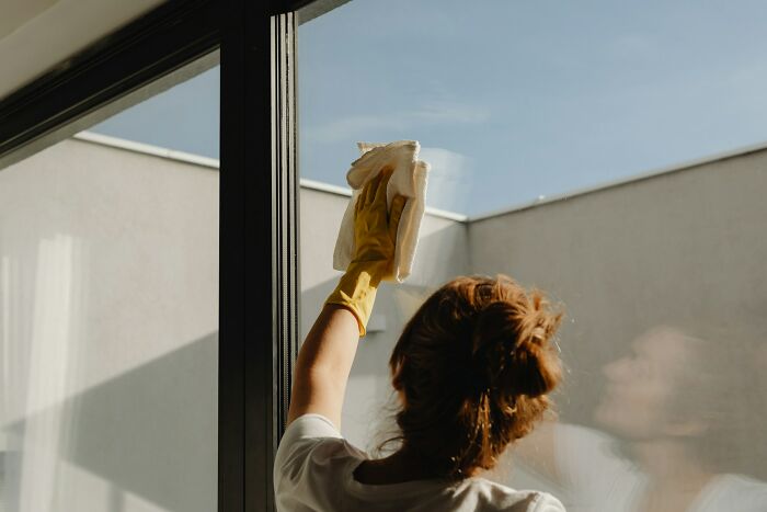 A person in yellow gloves cleaning a large window, a silent luxury many rich people enjoy.