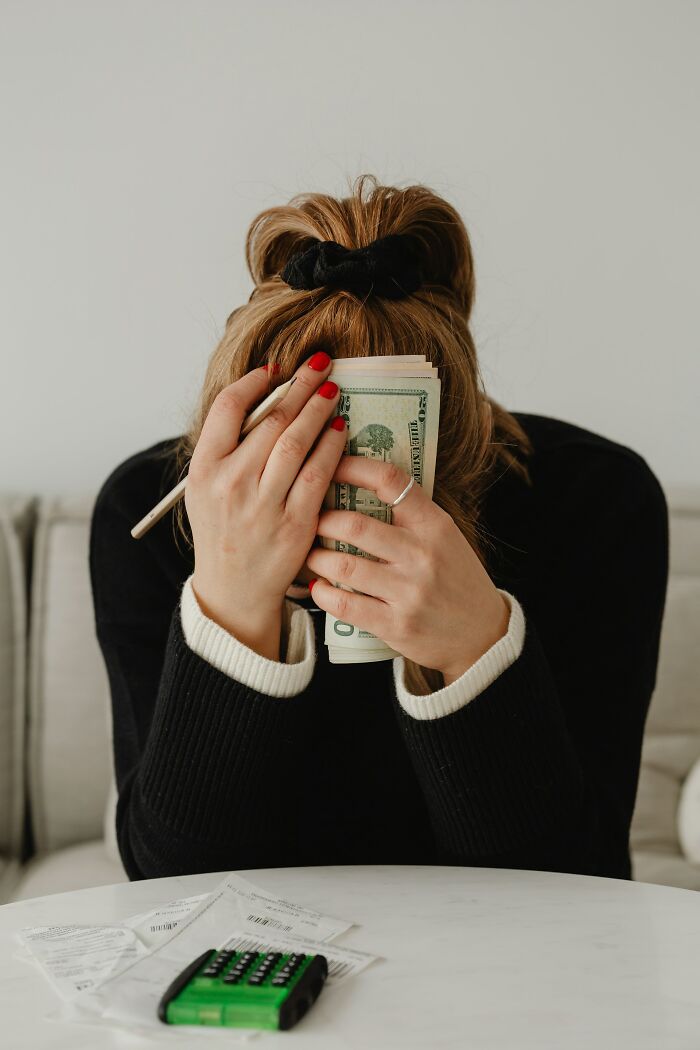 A woman with money covering her face, with bills and a calculator nearby, indicating financial wedding drama stories.