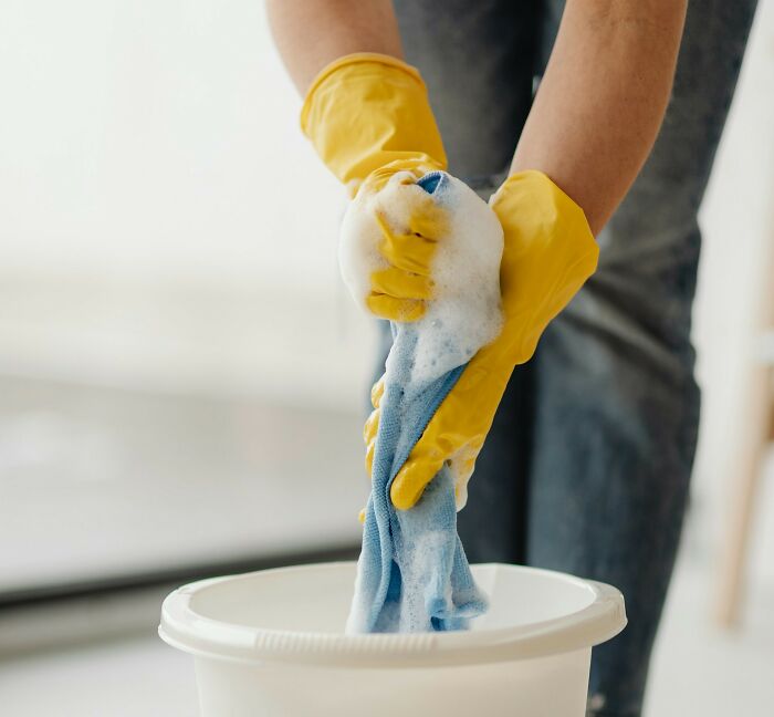 Person wearing yellow gloves wringing soapy cloth in bucket