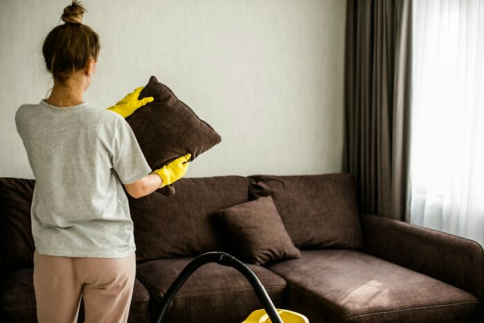 Hotel worker cleaning couch with gloves in guest room