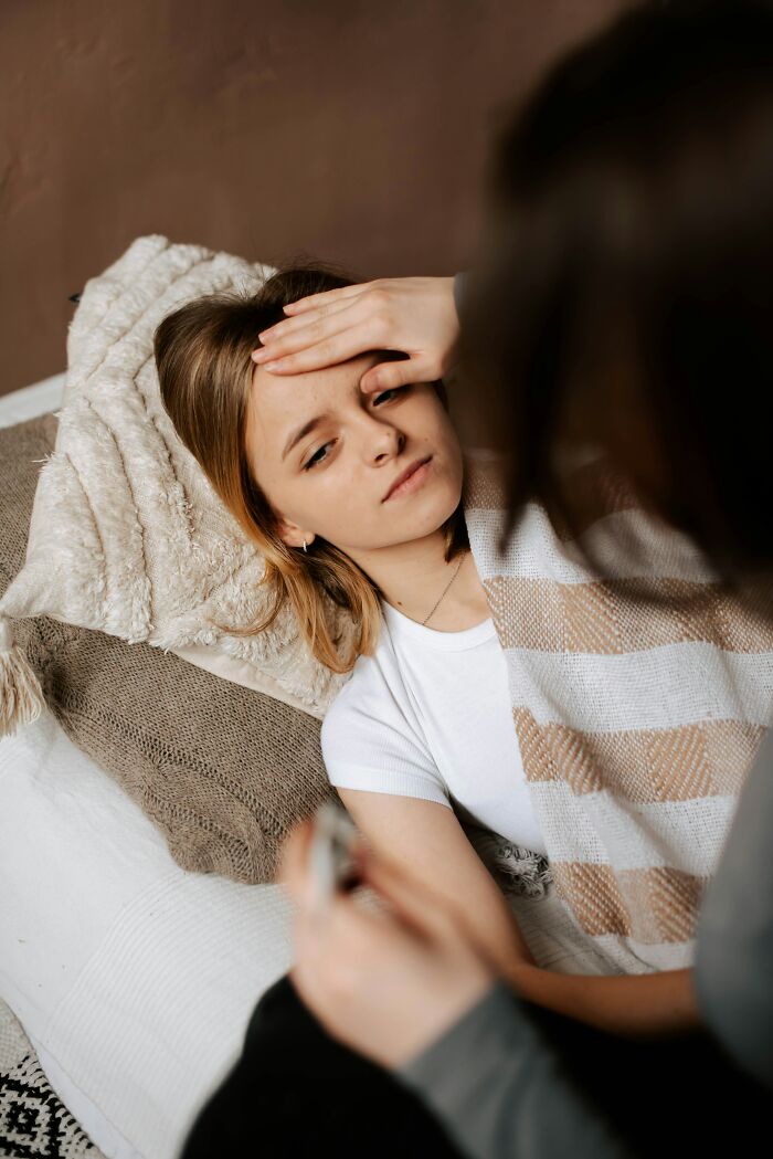 A person checking the forehead of another person lying down, possibly with a fever, highlighting health warning signs for routine cancer screening.