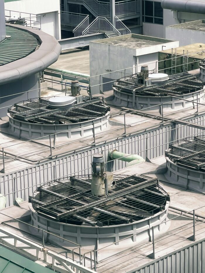 An aerial view of an industrial rooftop with multiple large cooling towers, steel pipes, and stairs. Disturbing d***h stories.