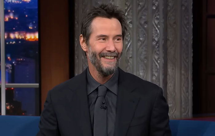 Keanu Reeves smiling during a late night interview wearing a black suit Keanu Reeves smiling during a late night interview wearing a black suit