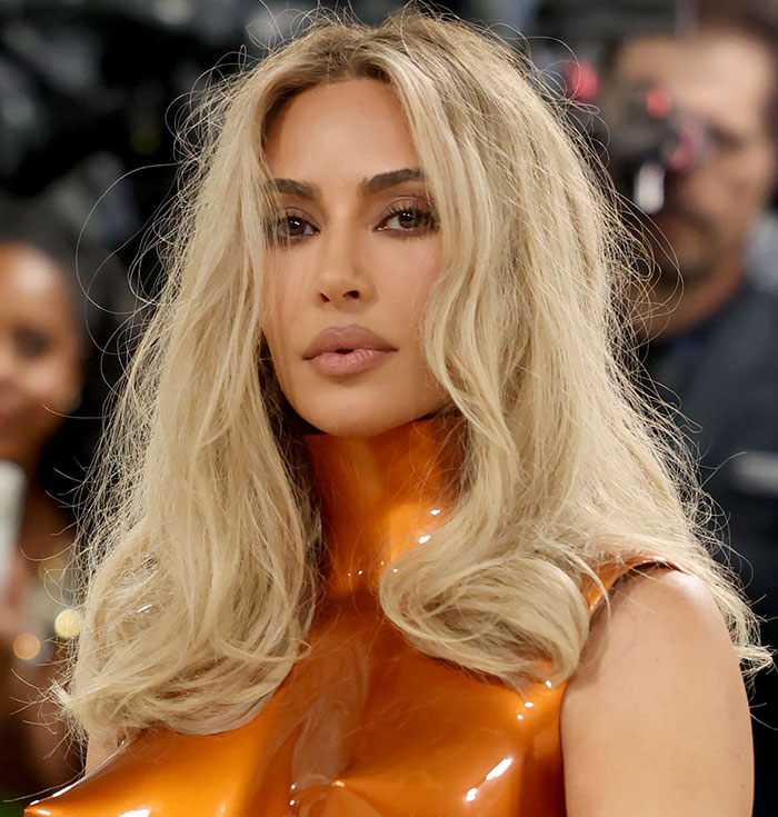 Close-up of a celebrity with blonde hair in an orange plastic top, highlighting how plastic surgery influences Met Gala fashion.