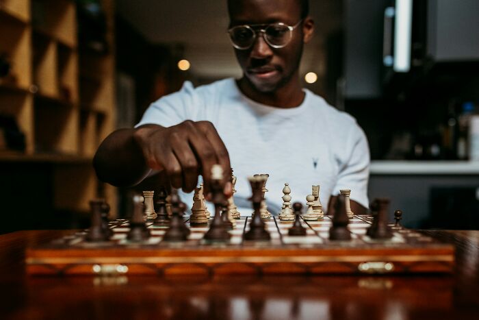 Man playing chess, moving a piece on a wooden chessboard indoors