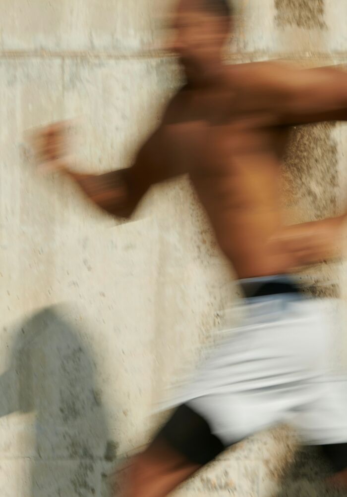Blurred motion of shirtless man running past stone wall