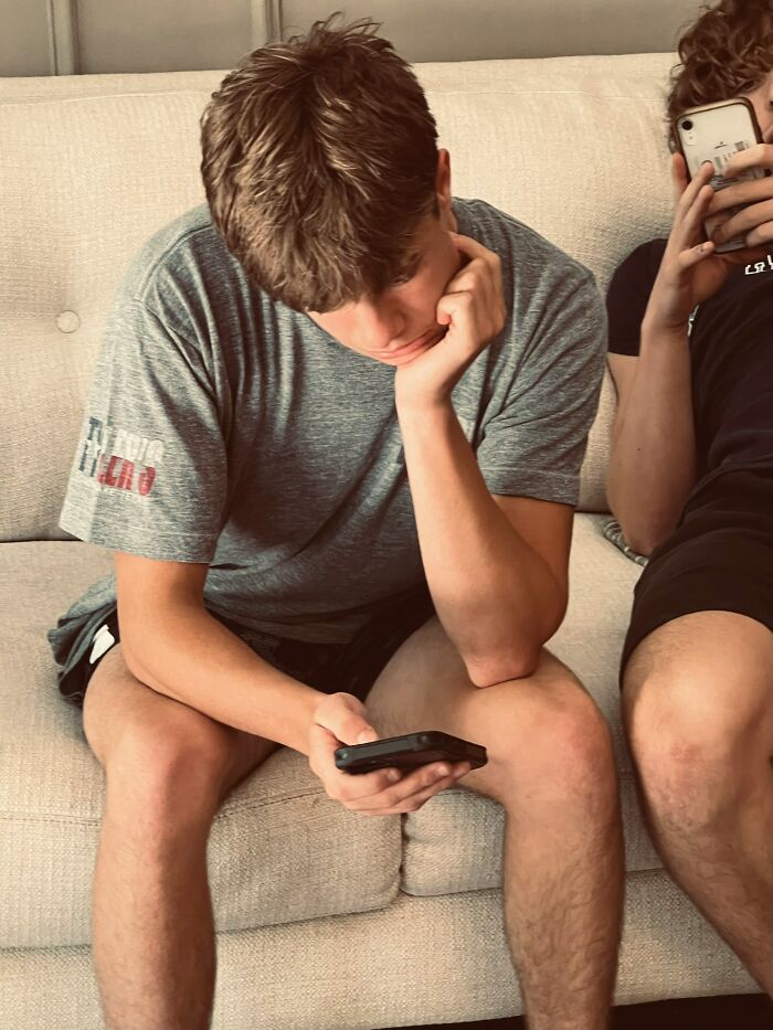A young man with brown hair intently looks at his phone while another holds their phone. This is typical Gen Z behavior.
