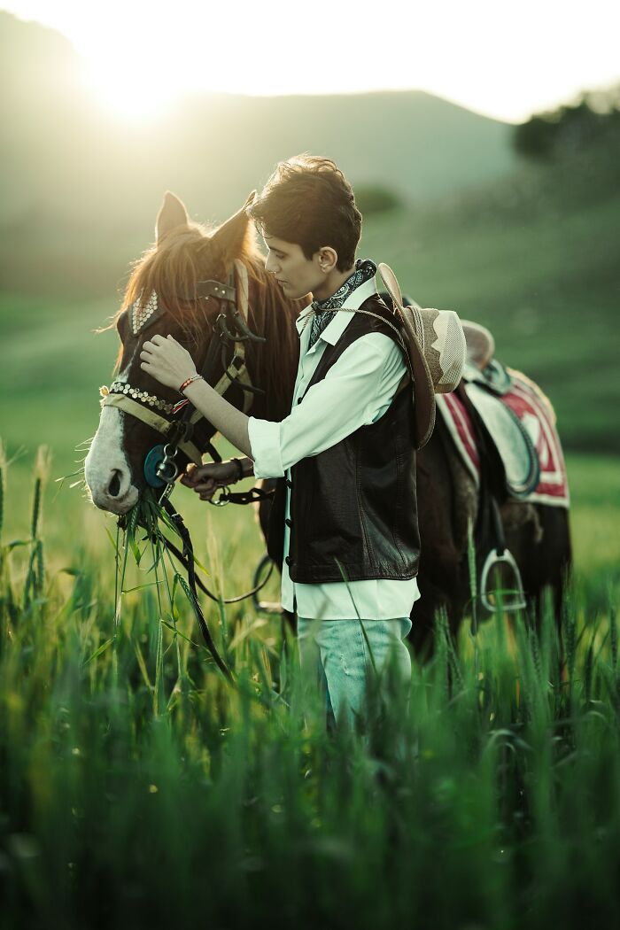 Young person feeding and petting horse in green field at sunset