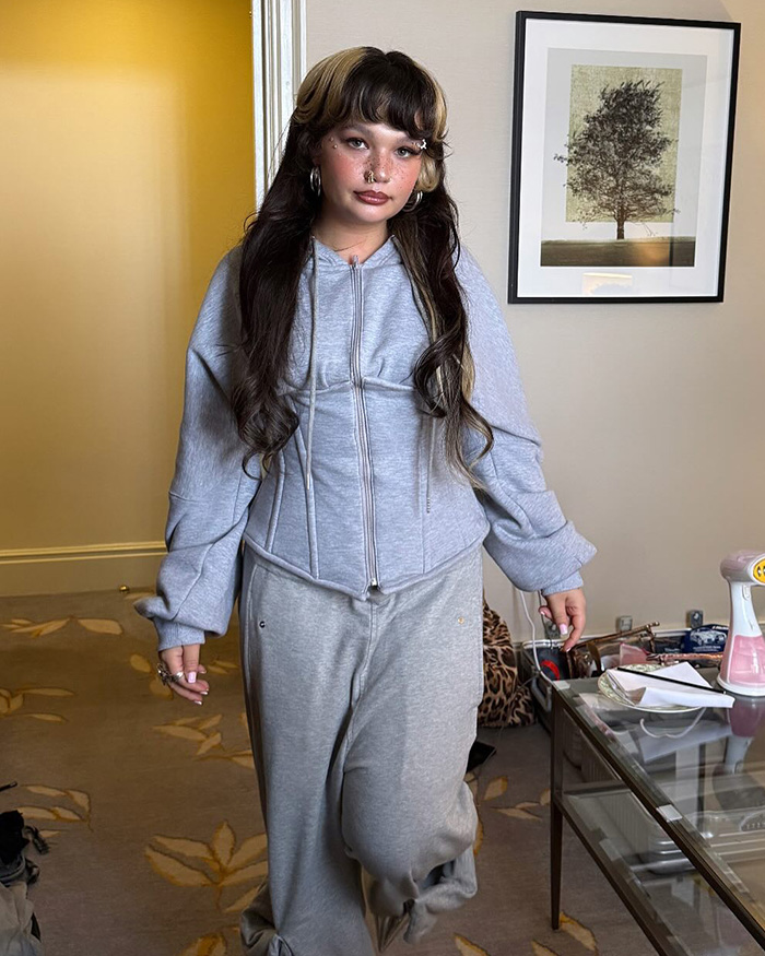 Lola Young, with long dark and blonde hair, wears a grey hoodie and sweatpants. Cheating Married Dad Lover.