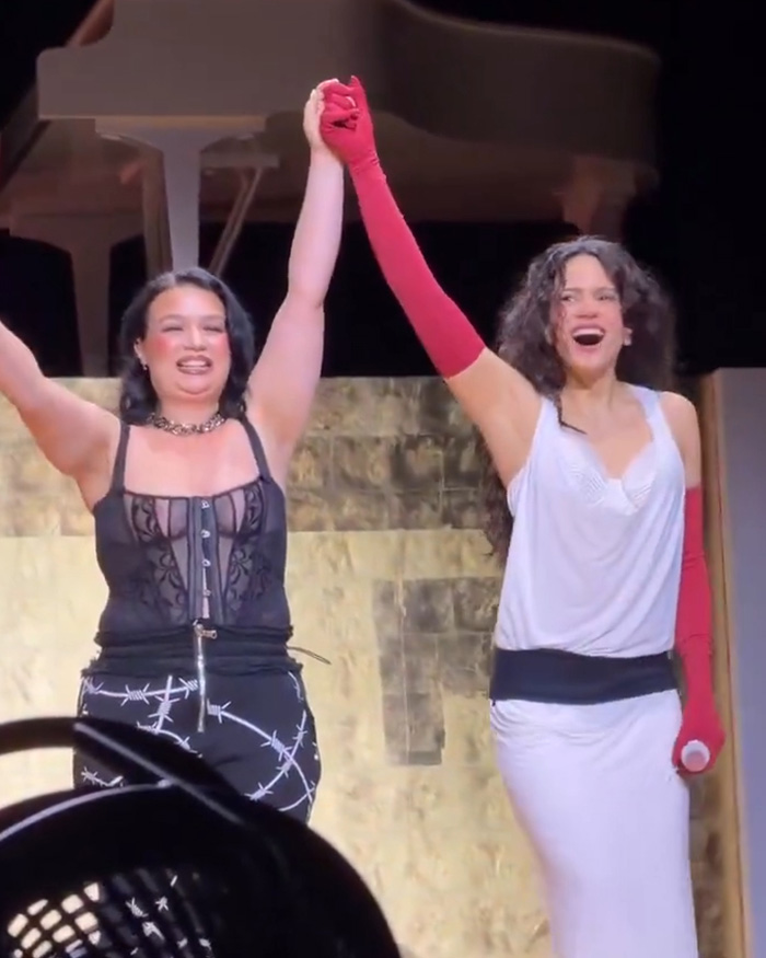 Lola Young and another woman raising their clasped hands on stage, celebrating. Lola Young cheating story.