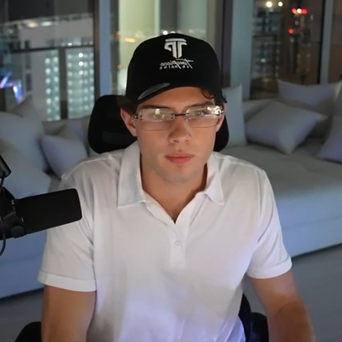 Looksmaxxing influencer wearing glasses and cap sitting indoors Looksmaxxing influencer wearing glasses and cap sitting indoors