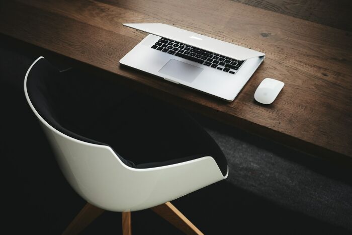 Modern workspace with an open laptop, mouse on a wooden desk. A white and black chair suggests epic comebacks ideas.