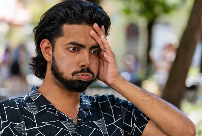 A man looks exasperated, hand on forehead, puffed cheeks, wearing a patterned shirt, illustrating the guy eating meat.
