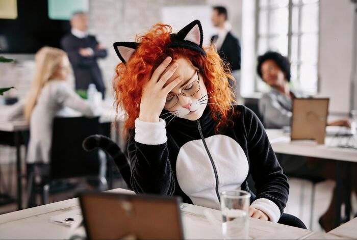 A person in a cat costume, facepalming at a desk, looking stressed, causing second-hand embarrassment in the office.