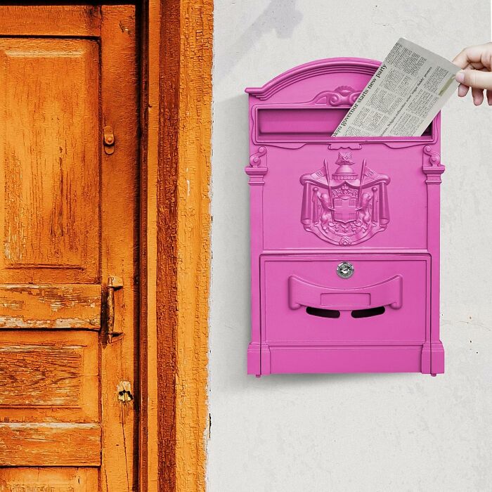 Hand inserting mail into a vibrant pink mailbox, next to a weathered orange door. Perfect for last minute Mothers Day gifts.