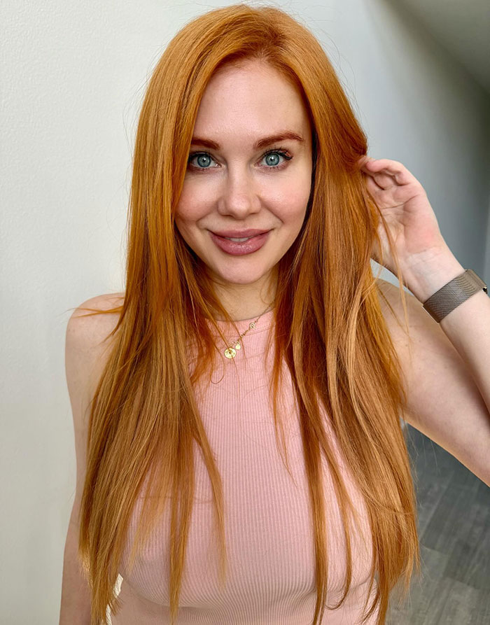 Former Disney star with long red hair wearing a pink top and smiling at the camera Former Disney star with long red hair wearing a pink top and smiling at the camera