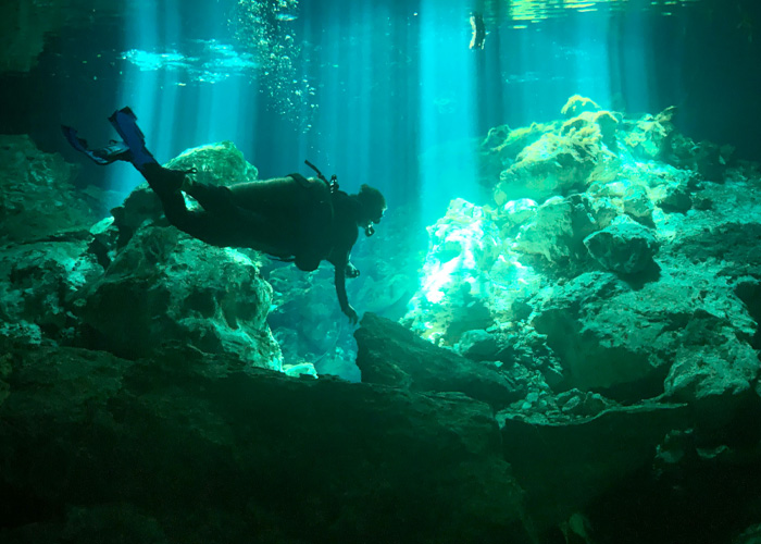 Mergulho subaquático na caverna das Maldivas com mergulhador explorando rochas em luz azul