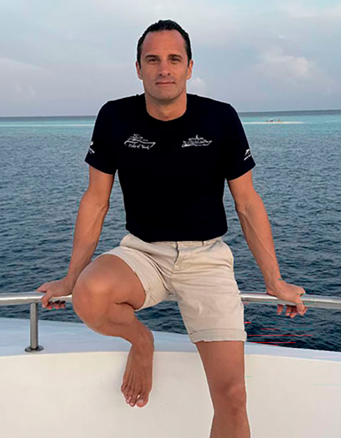 Homem de short e camiseta preta posando em um barco à beira-mar no mistério do mergulho em uma caverna nas Maldivas
