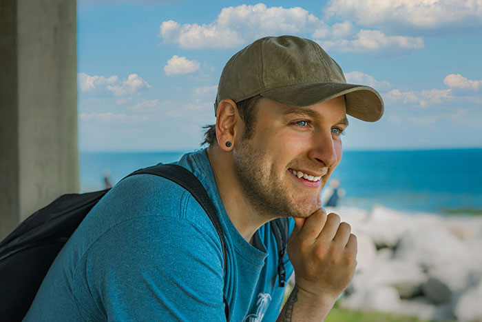 Man smiling outdoors wearing cap with ocean background
