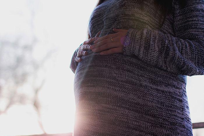 Close-up of a pregnant woman holding her belly in a knit sweater