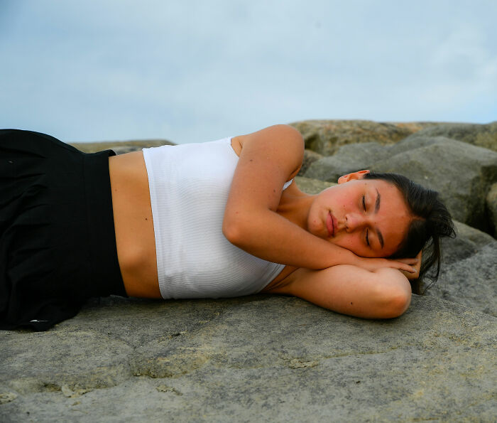 A young woman sleeping peacefully on rocks under a cloudy sky. Prioritizing routine cancer screening for health.
