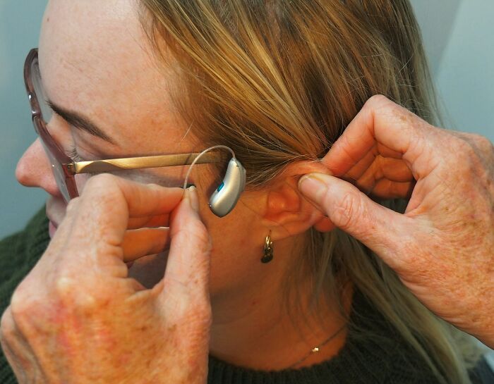 A woman with glasses getting a hearing aid adjusted behind her ear. Science professionals would find this fascinating.
