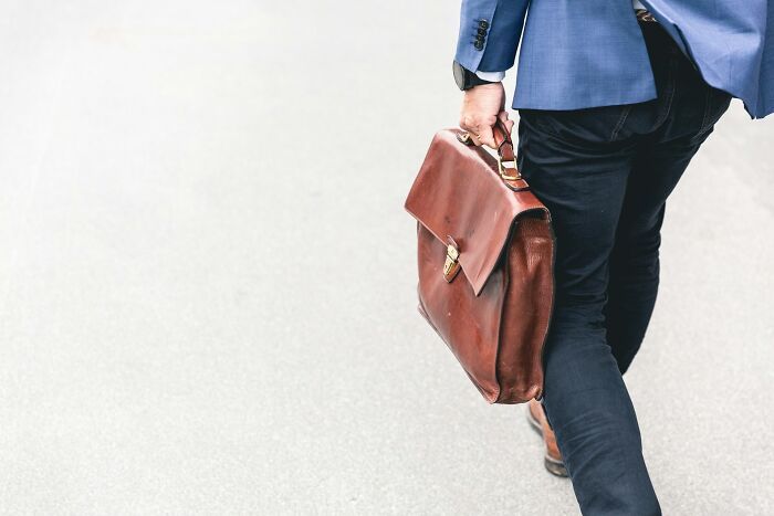 A person in a blue blazer and dark pants, carrying a brown leather briefcase, walking away. Represents epic comebacks.