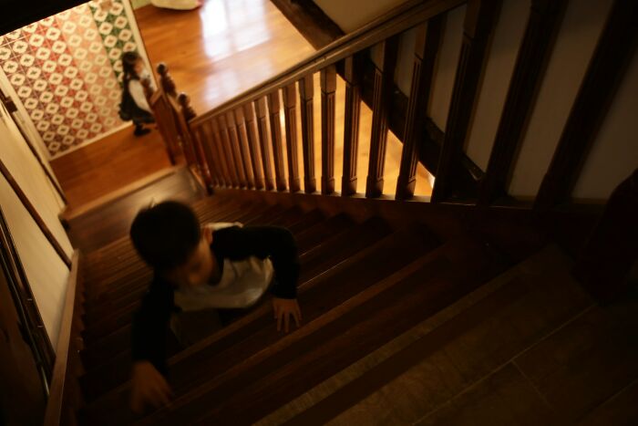 A young boy in a black and white shirt descends wooden stairs, with another person visible at the top. Engagement stories.