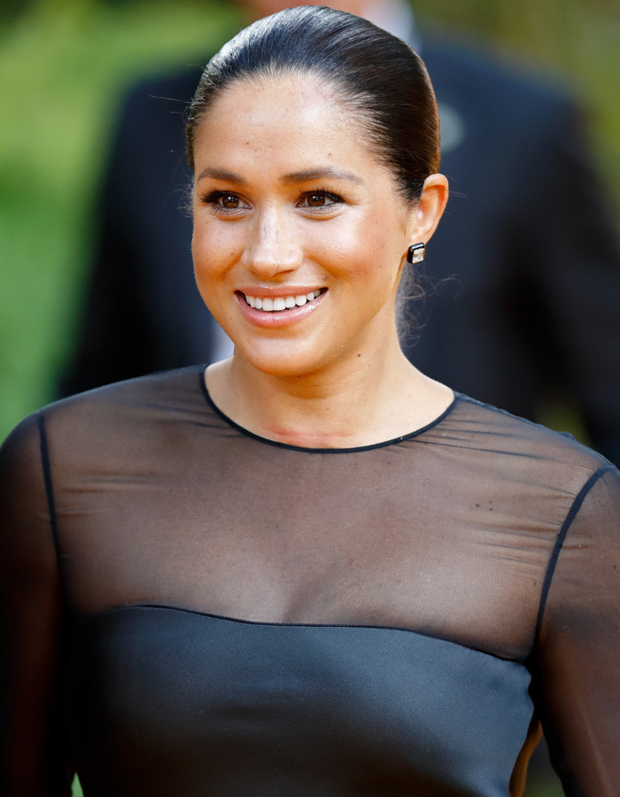 Close-up of Meghan Markle smiling in a black sheer top highlighting her appearance