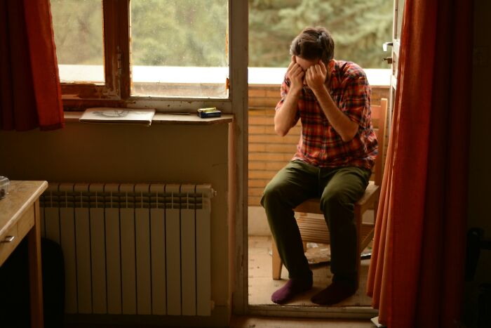 Man sitting indoors holding head showing fatigue or stress