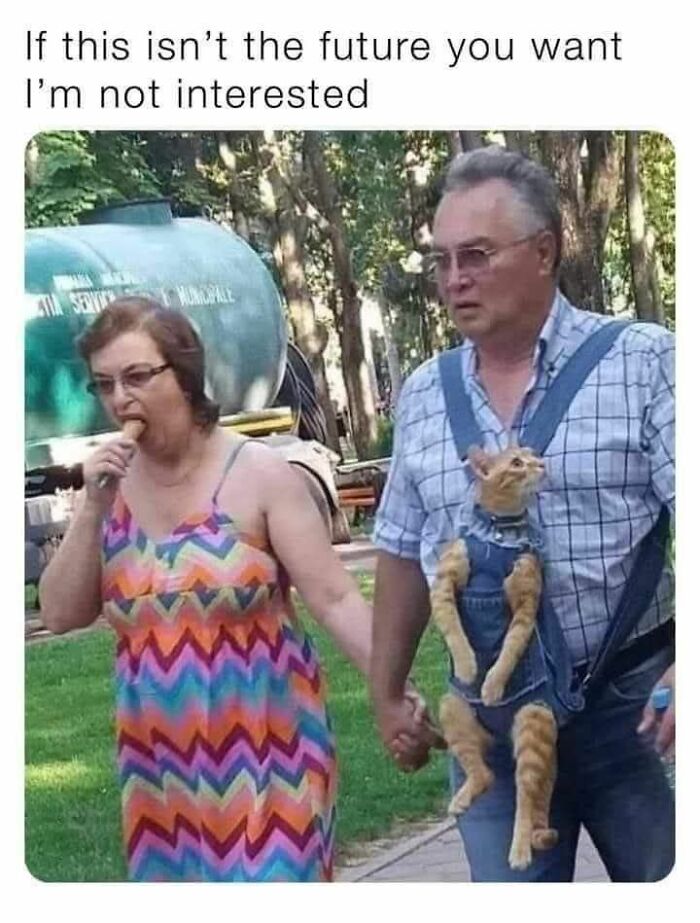 A woman eating a popsicle and a man holding a cat in a denim carrier, walking hand-in-hand, perfect for cat memes.