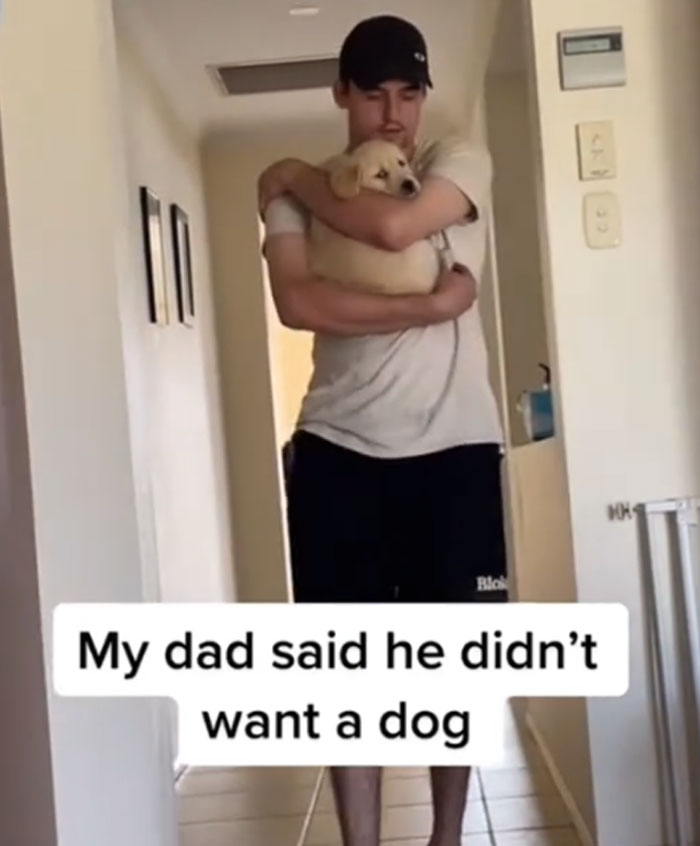 A man in a black cap and t-shirt, lovingly holding a golden retriever puppy. Men got a pet against their will.